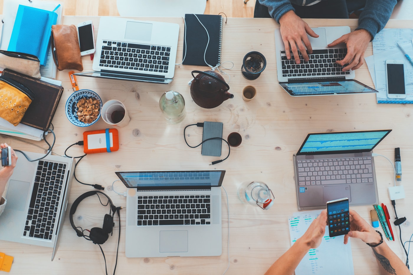 Overhead view of a shared desk with laptops, notebooks, and devices